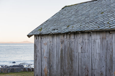 RUNDE, NORWAY - 2016 NOVEMBER 07. Old grey boat house with stone tiles on the roof.