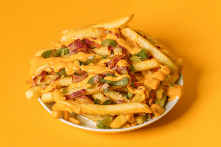Close up of a plate of loaded french fries with cheese, bacon and jalapeno on yellow background