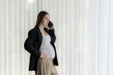 White pregnant woman talking on the phone. Pregnant businesswoman talking on the phone while working.の写真素材