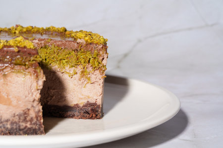 Close up chocolate cheesecake with pistachio paste and kataifi dough covered in chocolate ganache on white plate. White background with copy space. Indulgence, gourmet desserts, art of culinaryの写真素材