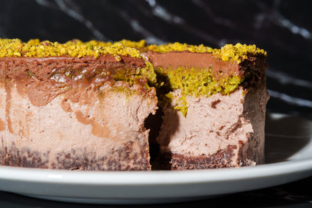 Slice of chocolate Dubai cheesecake with pistachio paste and kataifi dough filling covered in chocolate ganache on white plate. Close up. Indulgence, gourmet desserts, art of culinary presentationの写真素材
