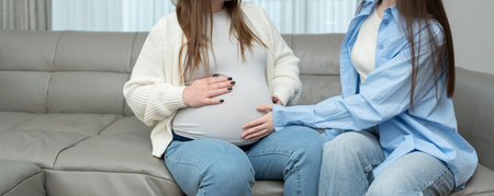 Banner of pregnant woman in third trimester sitting on sofa while her female friend touches her belly with care. Concept of maternity, friendship, connection, support and emotional bonding.の写真素材