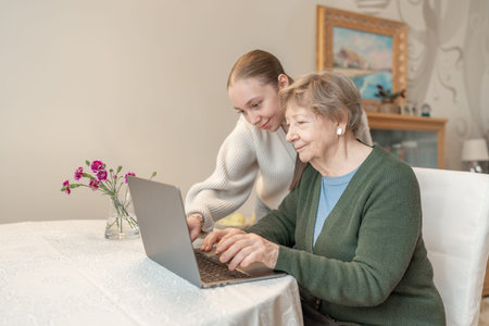 Young woman helping a senior woman with using laptop at home. Concept of technology, education, and...