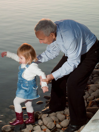 Girl toddler with grandfather by lake at sunset.の写真素材