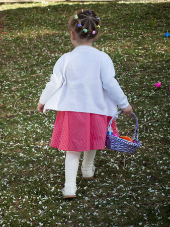 Little toddler girl on Easter egg hunt in urban park.