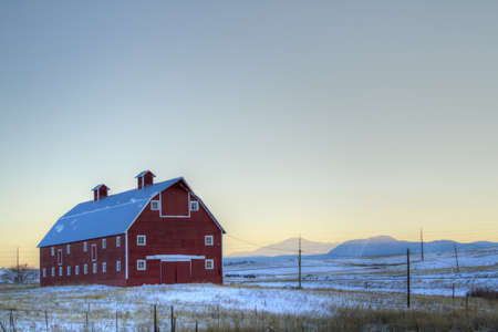 Red barn on the field covered in snow.のeditorial素材