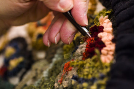 Hands work a hook in hug hooking craft.