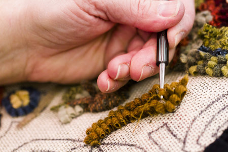 Hands work a hook in hug hooking craft.