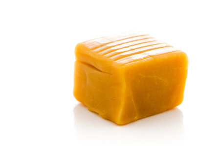 Vanilla caramel candy unwrapped on a white background.