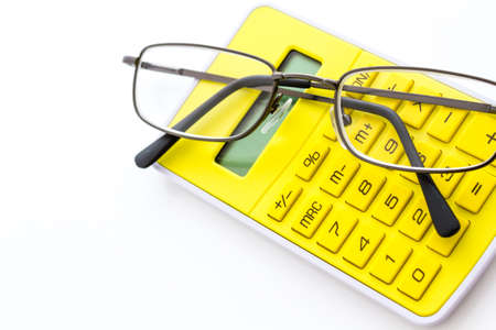 Simple yellow calculator with reading glasses on a white background.の写真素材