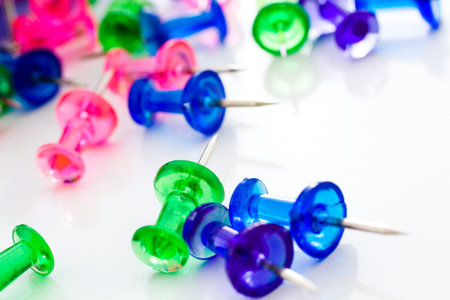 Multicolored thumbtacks in a pile on a white background.の写真素材