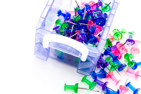 Multicolored thumbtacks in a pile on a white background.の写真素材