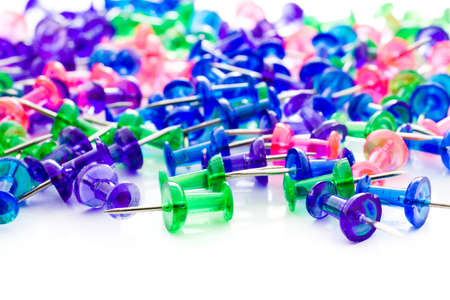 Multicolored thumbtacks in a pile on a white background の写真素材