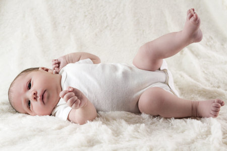 Newborn baby girl playing on a white blanket.