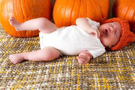 Newborn baby girl in orange pumpkin hat.