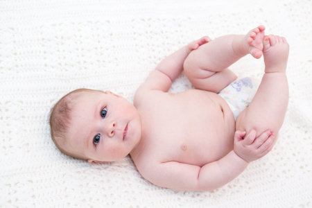 Infant baby girl playing on a white blanket.