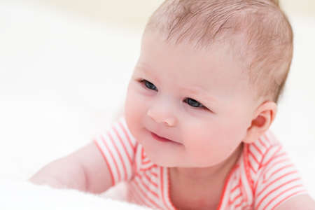 Infant baby girl playing on a white blanket.の写真素材