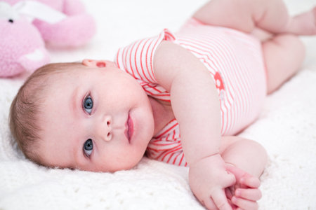 Infant baby girl playing on a white blanket.