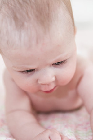 Infant baby girl playing on a pink blanket.