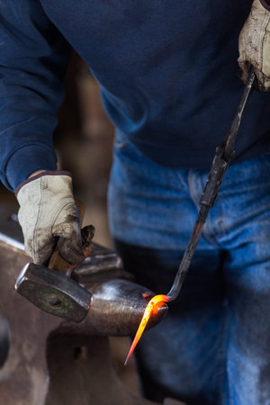 blacksmith bending hot iron on the anvil.