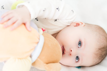 Baby girl playing with her teddy bear on a blanket.の写真素材