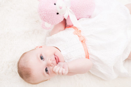 Baby girl in white dress playing on white blanket.