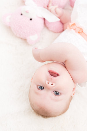Baby girl in white dress playing on white blanket.