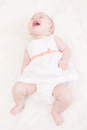 Baby girl in white dress playing on white blanket.