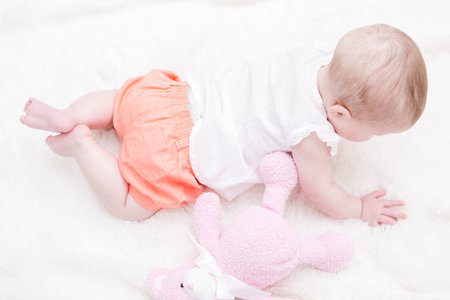 Cute baby girl playing on a white blanket.の写真素材