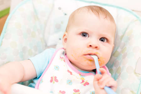 Little girl eating baby food in high chair.の写真素材