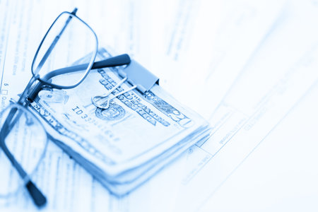 Calculating income tax return with folded cash on a table.