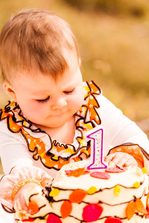 Baby girl celebrating her first bithday with gourmet cake and balloons.