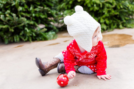 Cute baby girl in red Scandinavian dress at the Christmas tree farm.