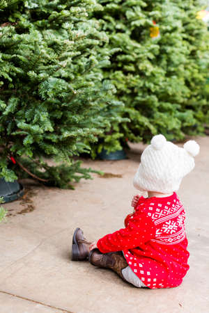 Cute baby girl in red Scandinavian dress at the Christmas tree farm.の写真素材