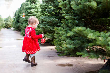 Cute baby girl in red Scandinavian dress at the Christmas tree farm.の写真素材