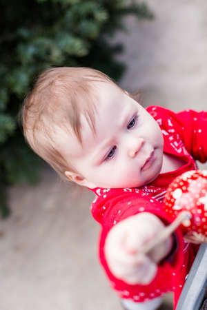 Cute baby girl in red Scandinavian dress at the Christmas tree farm.の写真素材