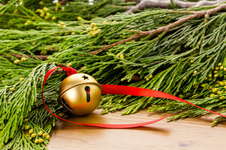Golden jingle bell with red ribbon on wood table.