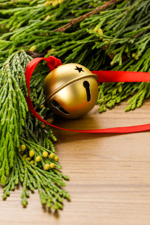 Golden jingle bell with red ribbon on wood table.