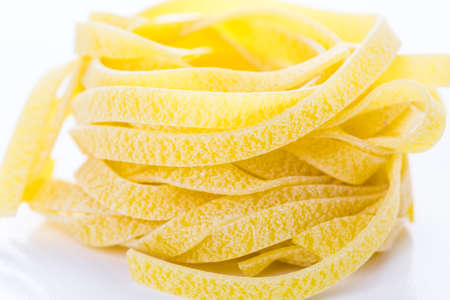 Organic yellow fettuccine nests pasta on a white background.の写真素材