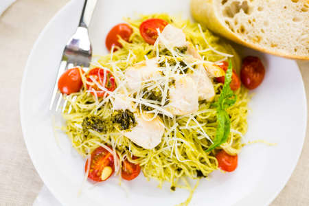 Homemade angel hair pasta with pesto sauce, roasted cherry tomatoes and grilled chicken.の写真素材