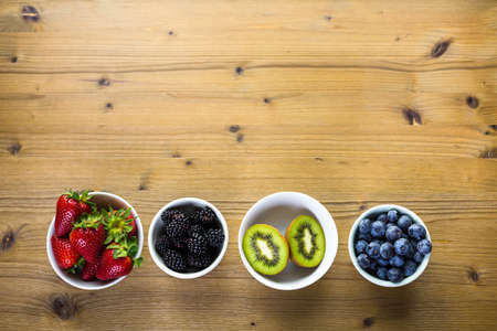 Organic fresh fruit in round bowls on wood table.の写真素材