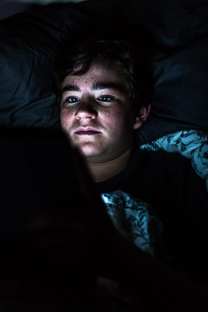Teenager boy on computer tablet in his room late at night.