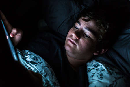 Teenager boy on computer tablet in his room late at night.の写真素材