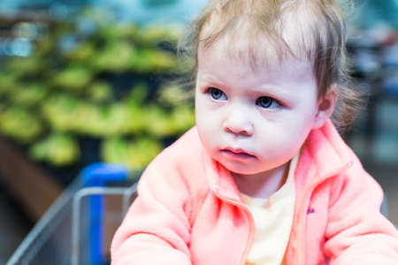 Cute toddler girl sitting in shopping cart at the grocery store.の写真素材