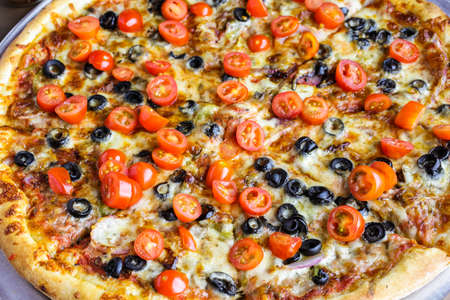 Veggie pizza with olives and cherry tomatoes on the table.の写真素材