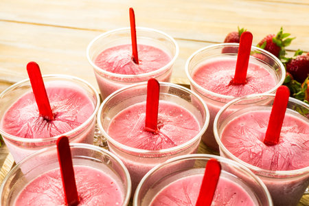 Homemade strawberry popsicles made in plastic cups.