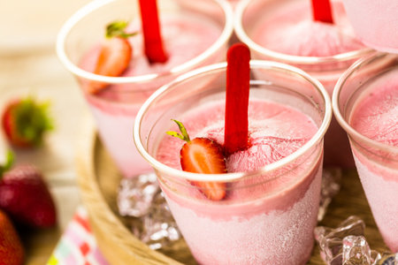Homemade strawberry popsicles made in plastic cups.