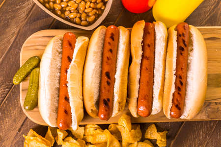 Grilled hot dogs on a white hot dog buns with chips and baked beans on the side.の写真素材