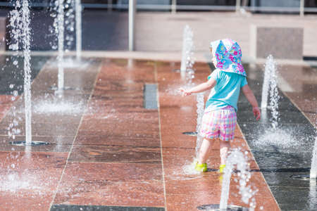 Cute toddler girl playing with small fountains in splash park.の写真素材