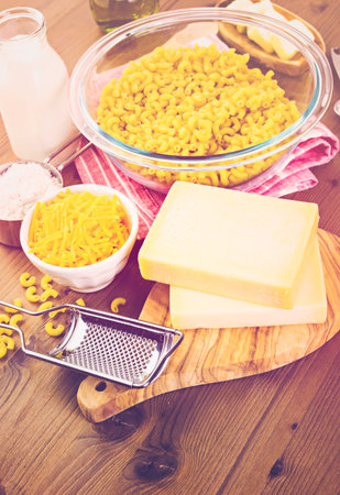Ingredients for preparing macaroni and cheese on a wood table.